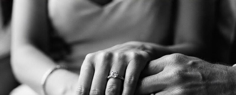 A black and white fine-art close-up of a couple holding hands.