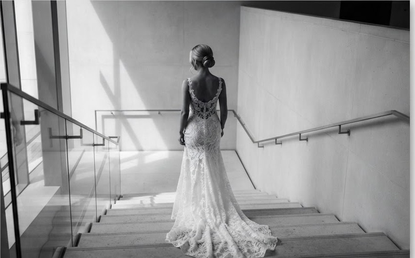 The back of a bride's lace dress as she walks down a grand staircase.